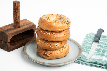 A Single Tall Stack Of Freshly Baked Bagels On A Ceramic Plate With Wood Cutting Stand And Knife