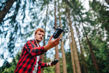 Man catches drone with his hand in the woods, close-up photo, focus on hands of the pilot. Guy launches a drone in flight with his hands on a background of trees. Drone flying in nature between trees
