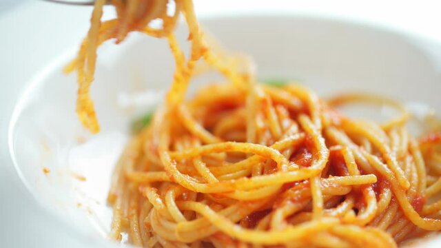 Closeup of eating a healthy plate of spaghetti pasta with tomato sauce, parmesan, and basil. Spinning macaroni with a fork. Italian food.