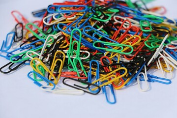 heap of colorful paper clips are lying on the white table