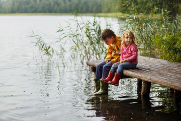 Brother and sister sitting on the river pier. happy children playing together . Boy and girl near lake