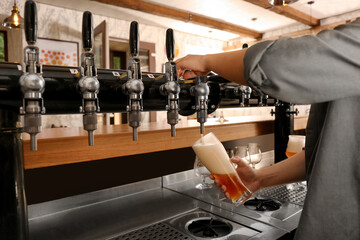 Bartender pouring fresh beer into glass in pub, closeup
