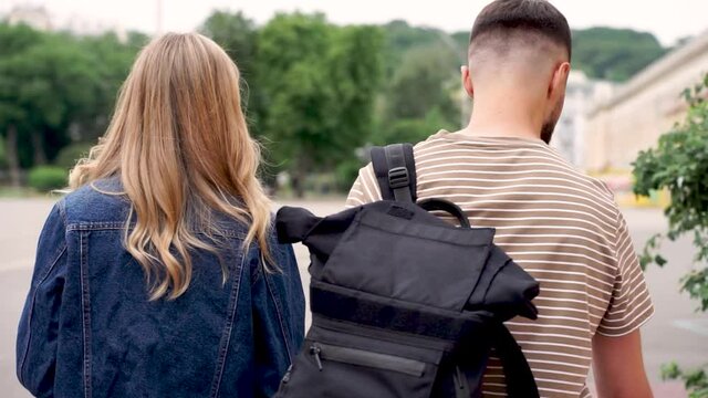 Two Young Students Walking Down The Street. View From Behind, Dolly Shot. Young Man And Woman.