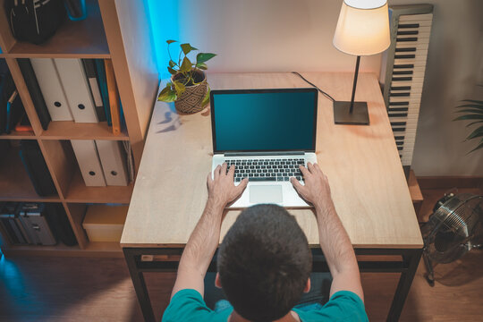 Shot from the back of a handsome male working at home with his laptop in his amazing work space. Mockup screen. Working from home. Hipster and modern work space.