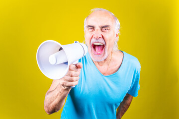 Senior man screaming loudly in a megaphone on yellow background -Elderly beautiful grey-haired man demonstrating using megaphone over isolated yellow background
