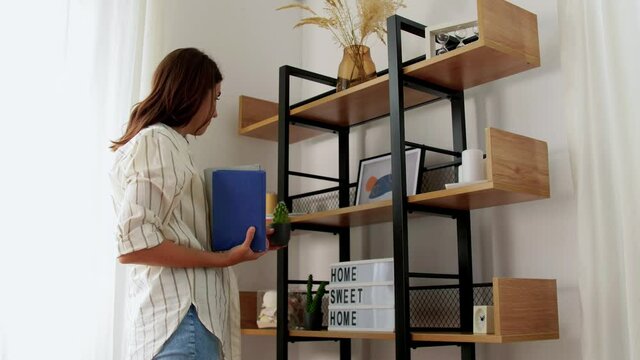 home improvement, decoration and people concept - woman arranging flowers, candles, books and other stuff on shelving