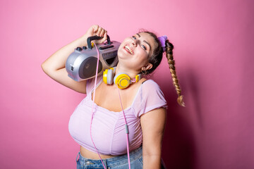 Young plus size woman on pink background dancing holding stereo - Chubby woman listening music...