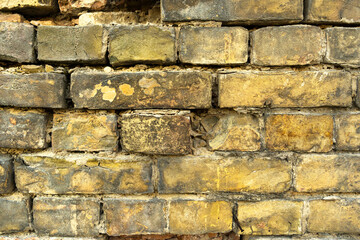 close-up of a very old crumbling wall made of yellow bricks.
