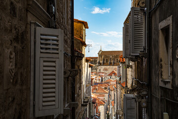 Ventanas blancas abiertas en callejón con fondo de tejados y cielo azul