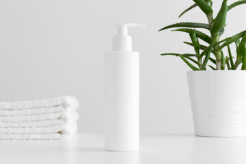 White cosmetic shampoo dispenser bottle mockup with a aloe vera and towels on a white table.