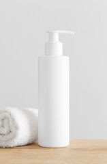 Fototapeta na wymiar White cosmetic shampoo dispenser bottle mockup with a towel on a wooden table.