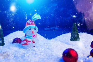 Snowman with Christmas balls on snow over fir-tree, night sky and moon. Shallow depth of field. Christmas background. Fairy tale. Macro. Artificial magic dreamy world