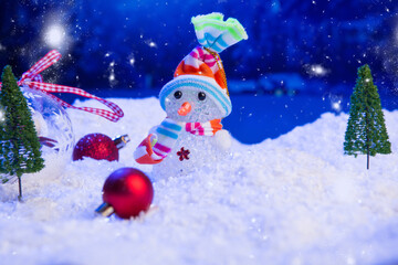 Snowman with Christmas balls on snow over fir-tree, night sky and moon. Shallow depth of field. Christmas background. Fairy tale. Macro. Artificial magic dreamy world