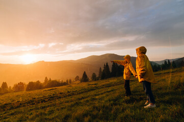 Two hiker hikers in the rain in the evening at sunset in the mountains. Two people in yellow...