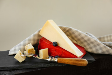 Different types of delicious cheeses and fork on slate plate, closeup