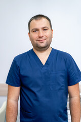 Fototapeta premium Portrait of a male doctor in hospital. Man looking at camera and smiling. White wall background. Closeup.