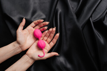female hands in handcuffs on a dark silk sheet with anal beads