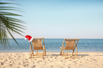Sun loungers and Santa's hat on beach, space for text. Christmas vacation