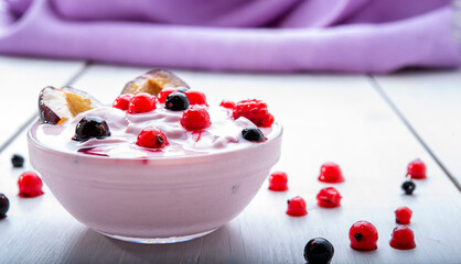 Bowl of yogurt and  berries on white wooden background violet napkin on background