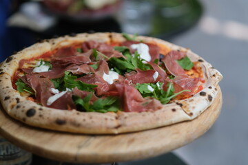 close up pizza with cured meats, arugula and cheese. On wooden plate. Defocused background