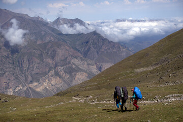 Obraz premium Backpackers trekking in mountains. Tourists hike through the valley. Valley near Bulungu village.