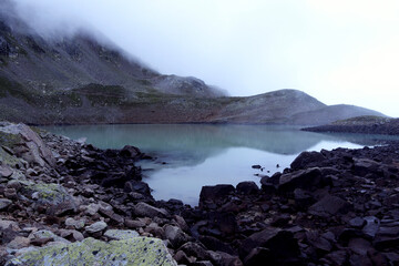 Alpine lake in the clouds. Alpine lake with rocky shores and emerald water in the clouds. Alpine lake Giybashkel (3240 meters above sea level), Caucasus. 