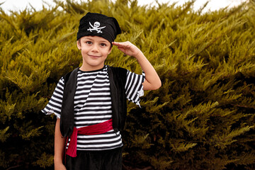 Cute boy in pirate costume standing by bushes