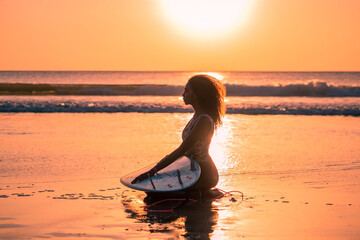 Fototapeta premium Portrait of woman surfer with beautiful body on the beach with surfboard at colorful sunset.