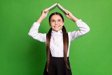 Photo portrait of happy schoolgirl holding open book over head isolated on vivid green colored...