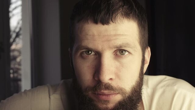 Close-up face without emotion. Handsome bearded caucasian guy looking at the camera. 4K