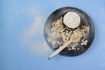 Organic uncooked oatmeal grains on plate, oat flour in bowl, blue background. Healthy concept. Top view. Copy space.