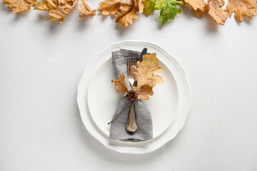 Elegant fall table setting with dry leaves and white plate on white table.