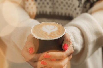Female hands in sweater holding a cup of latte coffee
