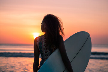 Fototapeta na wymiar Portrait of woman surfer with beautiful body on the beach with surfboard at colorful sunset.