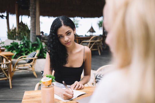 Portrait of serious brunette female journalist noting information in notepad during interviewing woman,cropped image of hipster girl having meeting for cooperating and planning project together