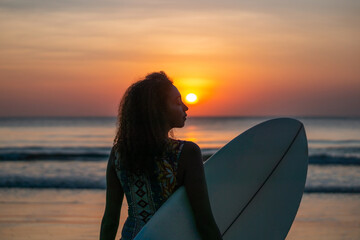 Fototapeta na wymiar Portrait of woman surfer with beautiful body on the beach with surfboard at colorful sunset