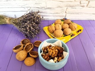 Walnuts whole and split, a sprig of lavender and a blue Cup with peeled nuts on a purple background