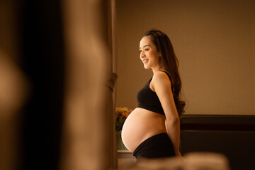 portrait of a pregnant woman touching her belly on the foreground in emotional smile happy by asian woman