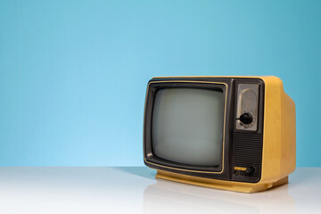 Old retro yellow TV receiver set on white table on blue background