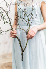 Girl in a blue chiffon lace dress holding dead tree branch with moss, Shallow dwepth of field hands...