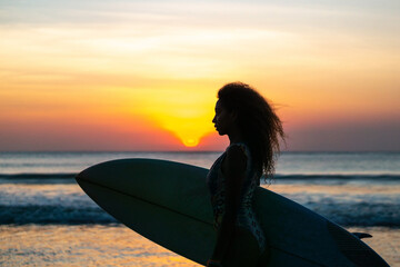 Portrait of woman surfer with beautiful body on the beach with surfboard at colorful sunset