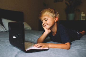 child does homework , lying in bed using his laptop or skyping.