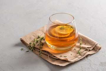 Hot tea in a glass with lemon and thyme on a linen napkin, gray background with copy space. Autumn and winter traditional drinks.