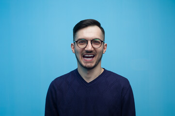 Portrait of an emotional young man in glasses shocked by low prices and discounts on a blue background.