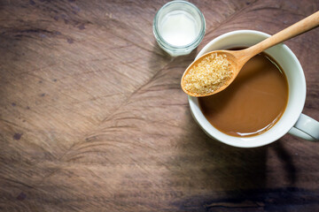 Cup of coffee with brown sugar and milk on wooden background.