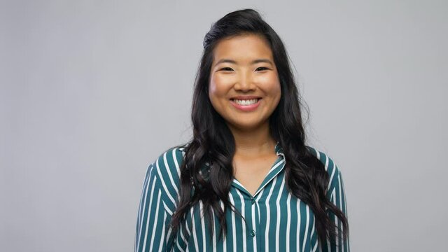 people, ethnicity and portrait concept - happy asian young woman over grey background