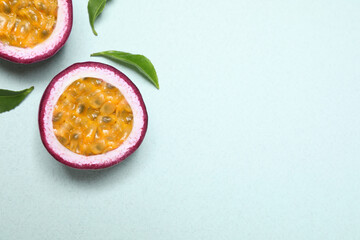 Halves of fresh ripe passion fruit (maracuya) with leaves on light background, flat lay. Space for...