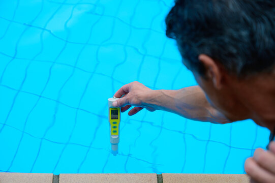 man holds an electronic device to check the pH of the water in the pool and the disinfection of the water against covid 19