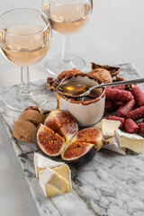 Brie and cheese with paprika, salami, figs, walnuts, honey and rose wine on a marble board. Food for a romantic date on a light concrete background. Top view