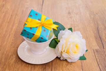 A small gift box on cup of coffee with A single white Rose lying down on wooden background. Copy space